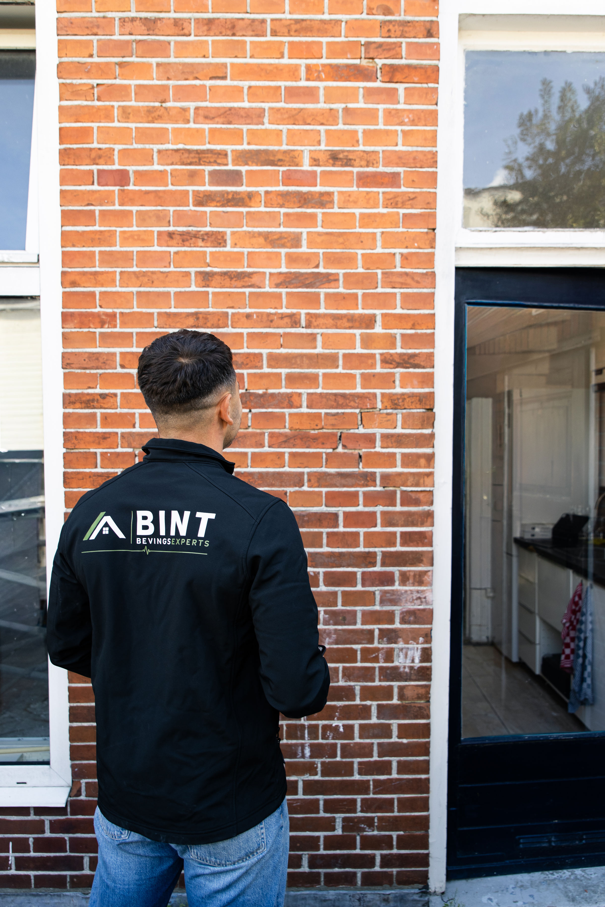 Een medewerker van BINT bekijkt scheuren in de bakstenen achtergevel van een woning