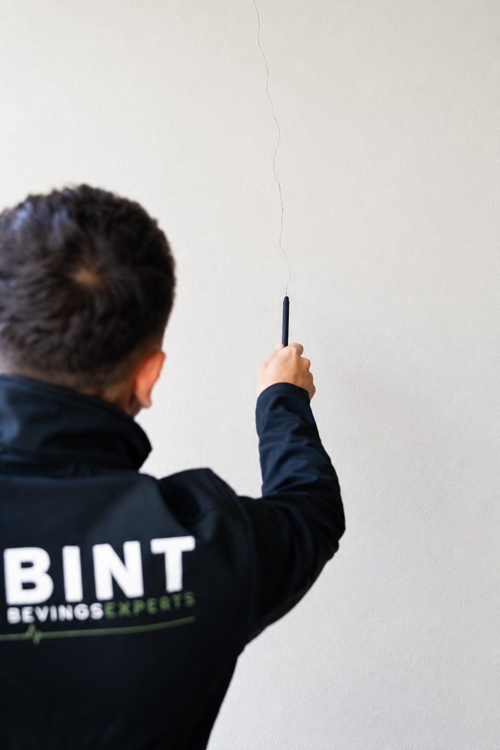 Een medewerker van BINT wijst naar een fijne scheur in een gestucte wand